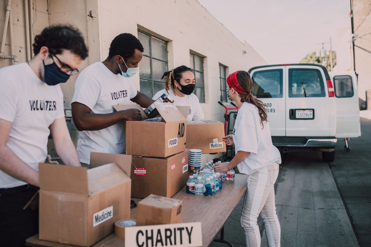 services-01 Group of volunteers wearing masks packing charity boxes outdoors during the pandemic.